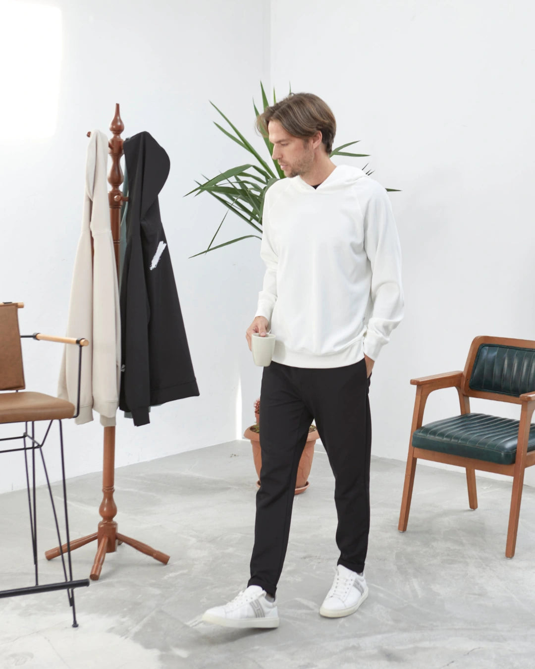 MUBU İstanbul erkek günlük giyim koleksiyonundan zamansız tasarıma sahip beyaz kapüşonlu sweatshirt ve siyah jogger pantolon kombiniyle yürüyen erkek model.